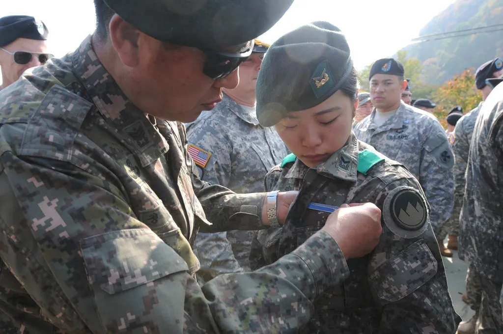 A South Korean woman soldier in camouflage uniform has a badge pinned on her chest at an outdoor ceremony