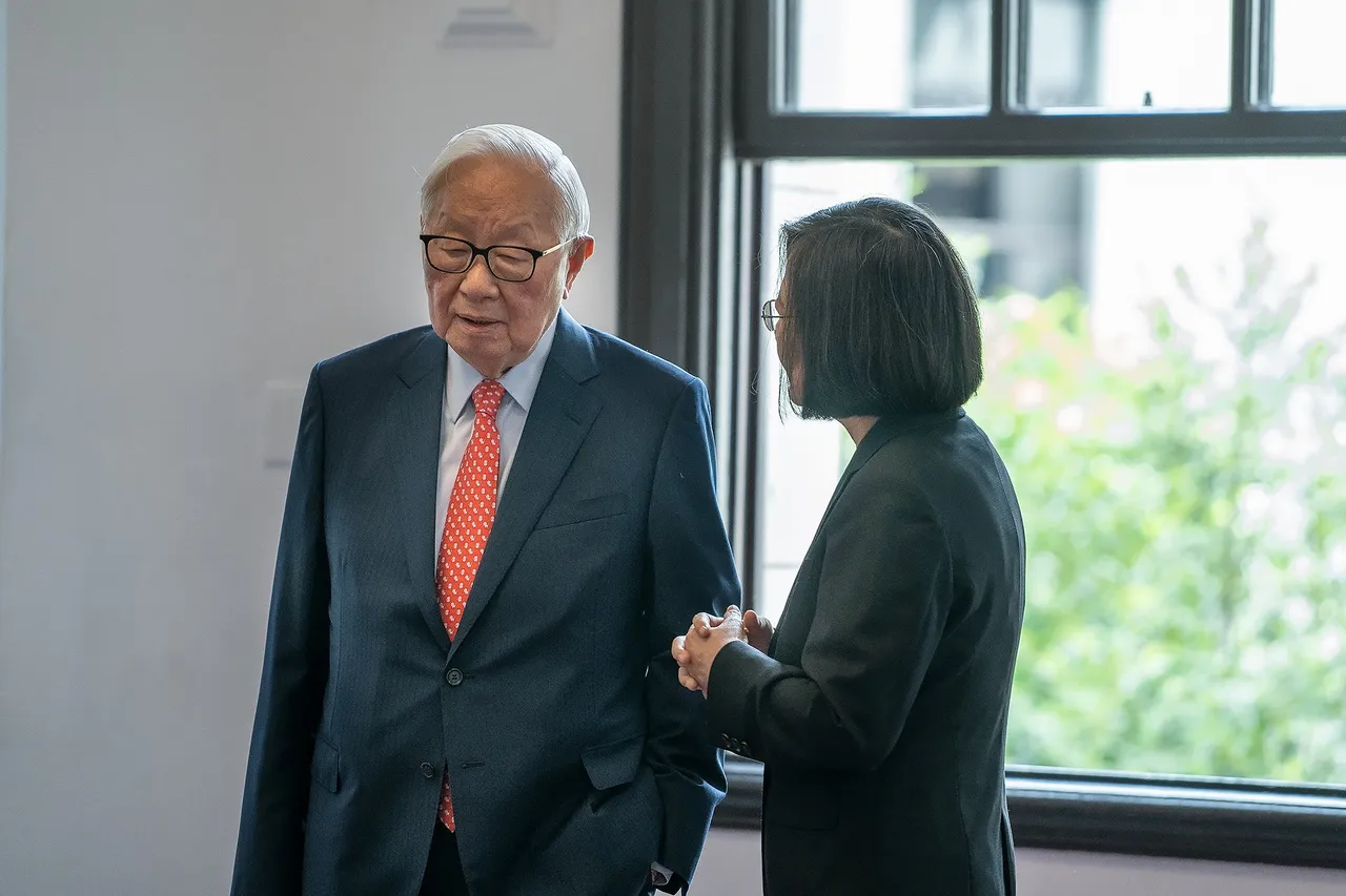 Tsai Ing-wen, in a dark suit, talks with Morris Chang, an older man in glasses and a red tie, beside a window.