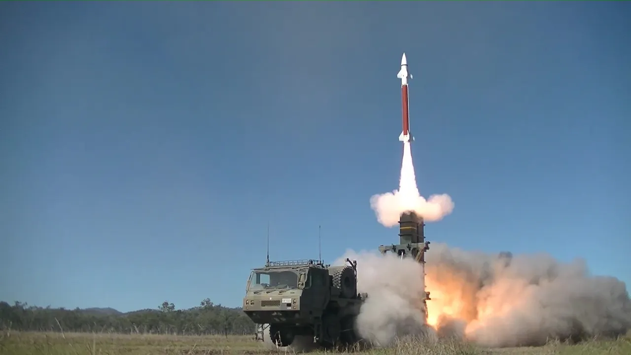 A Japanese Type 03 surface-to-air missile launches from a truck-mounted launcher amid smoke on a grassy range under a blue sky.