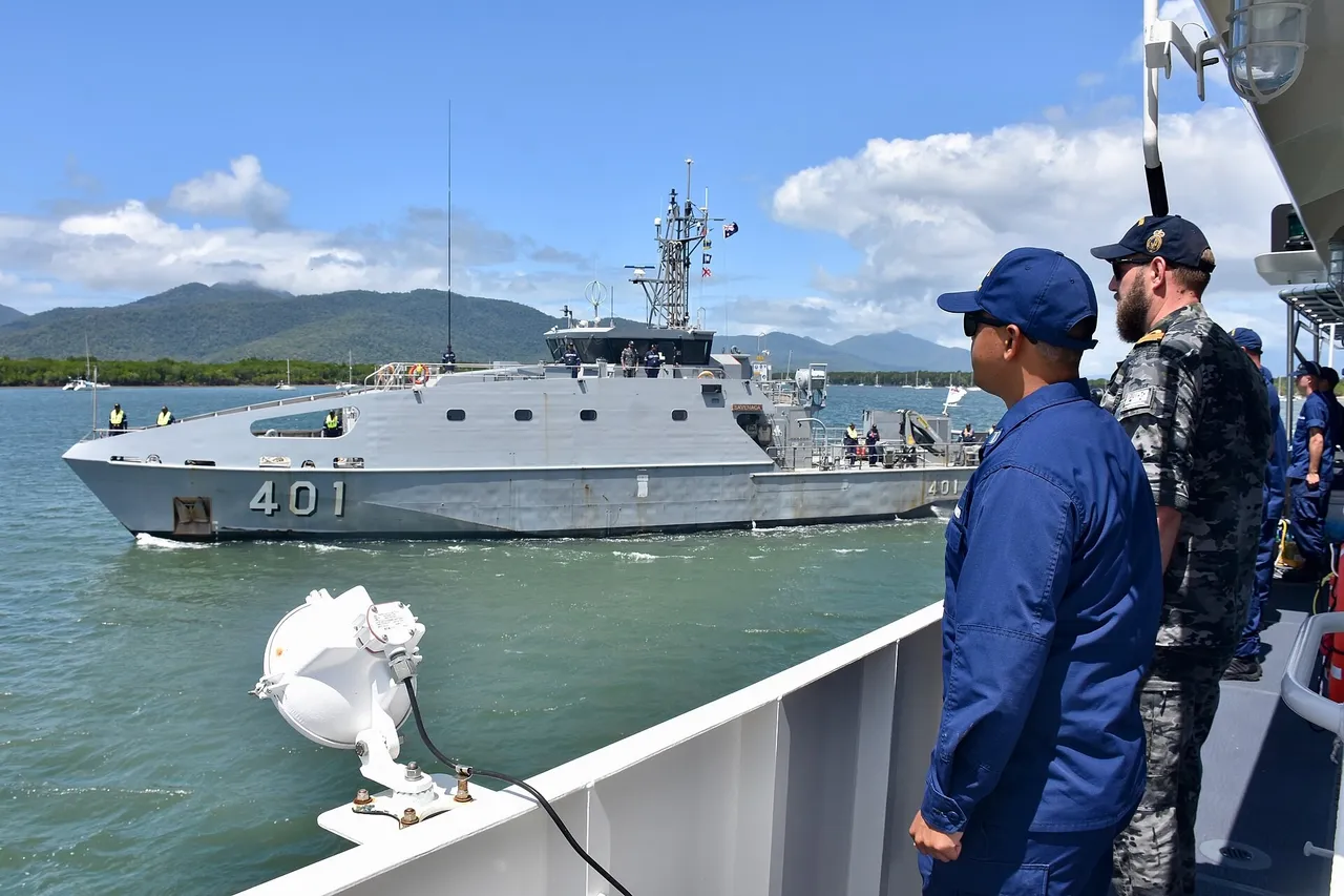 A grey Fijian navy patrol boat numbered 401 sails past a ship on which a US Coast Guard sailor and an Australian sailor stand watching