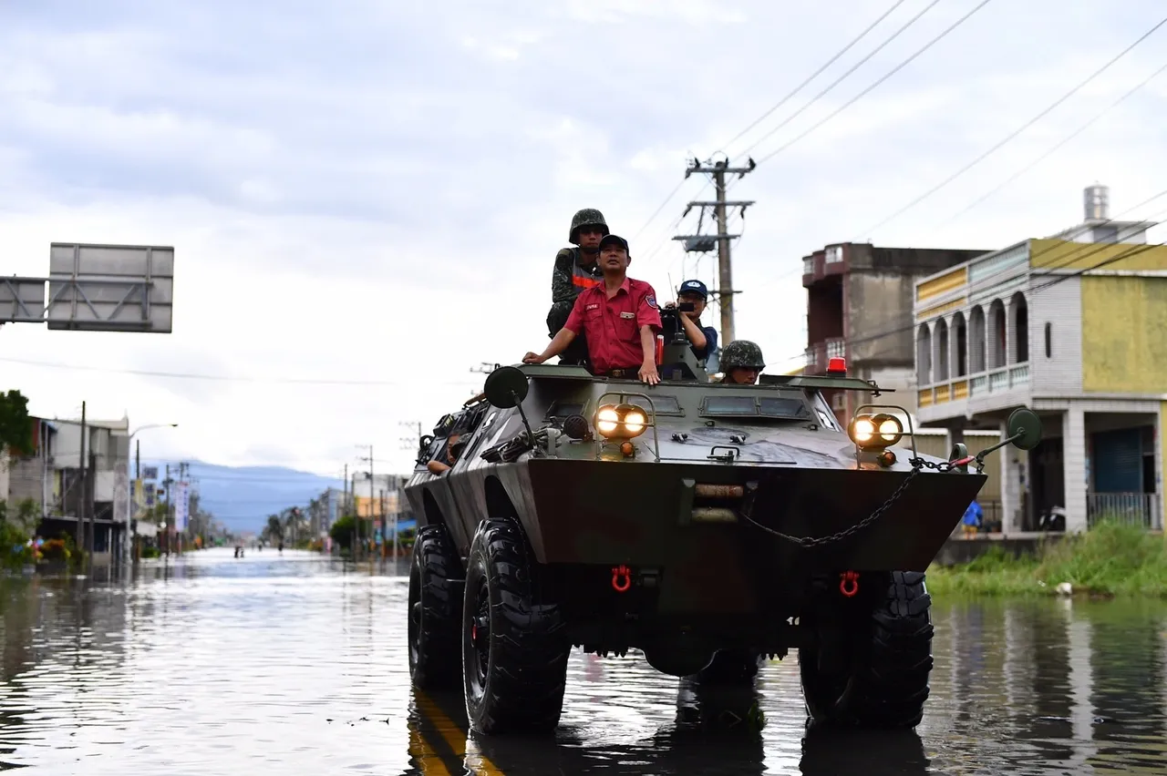 Soldiers and a relief worker ride on top of a military armoured vehicle driving through a flooded town street