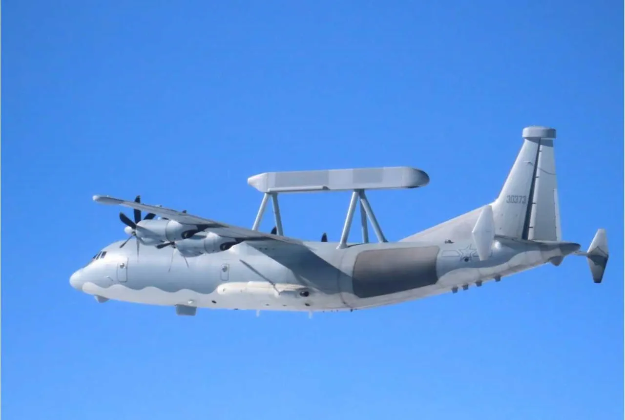 A grey four-propeller Chinese military aircraft with a long flat radar antenna mounted on top of its fuselage, flying over the sea.