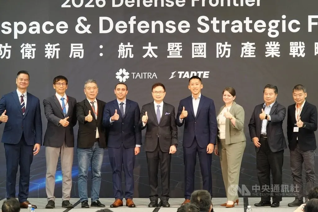 Nine people in business attire give a thumbs-up on stage in front of a banner reading Aerospace and Defense Strategic Forum with TAITRA and TADTE logos.