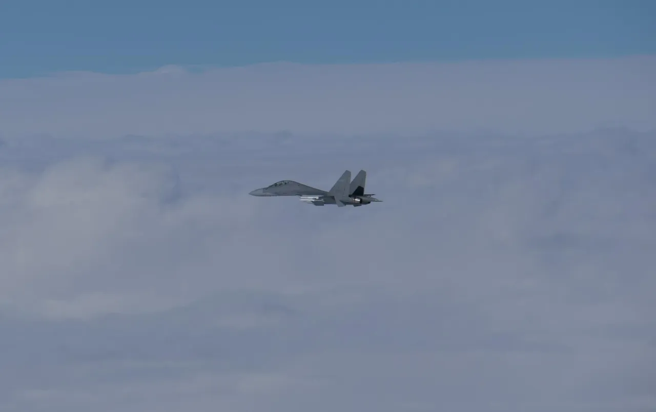 A grey Chinese J-16 twin-engine fighter jet flying above a layer of white cloud