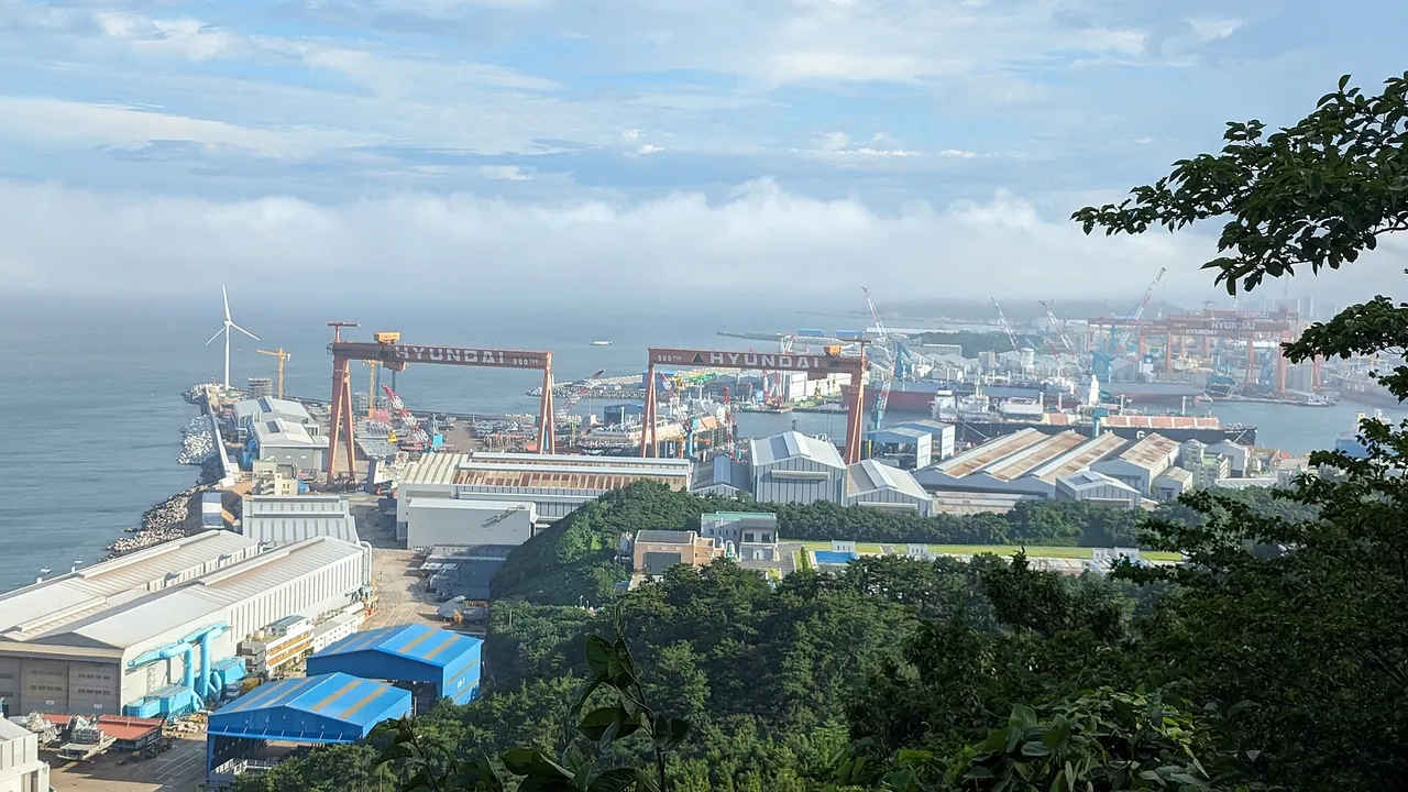Large shipyard on the coast with several red gantry cranes and ships under construction beside the sea