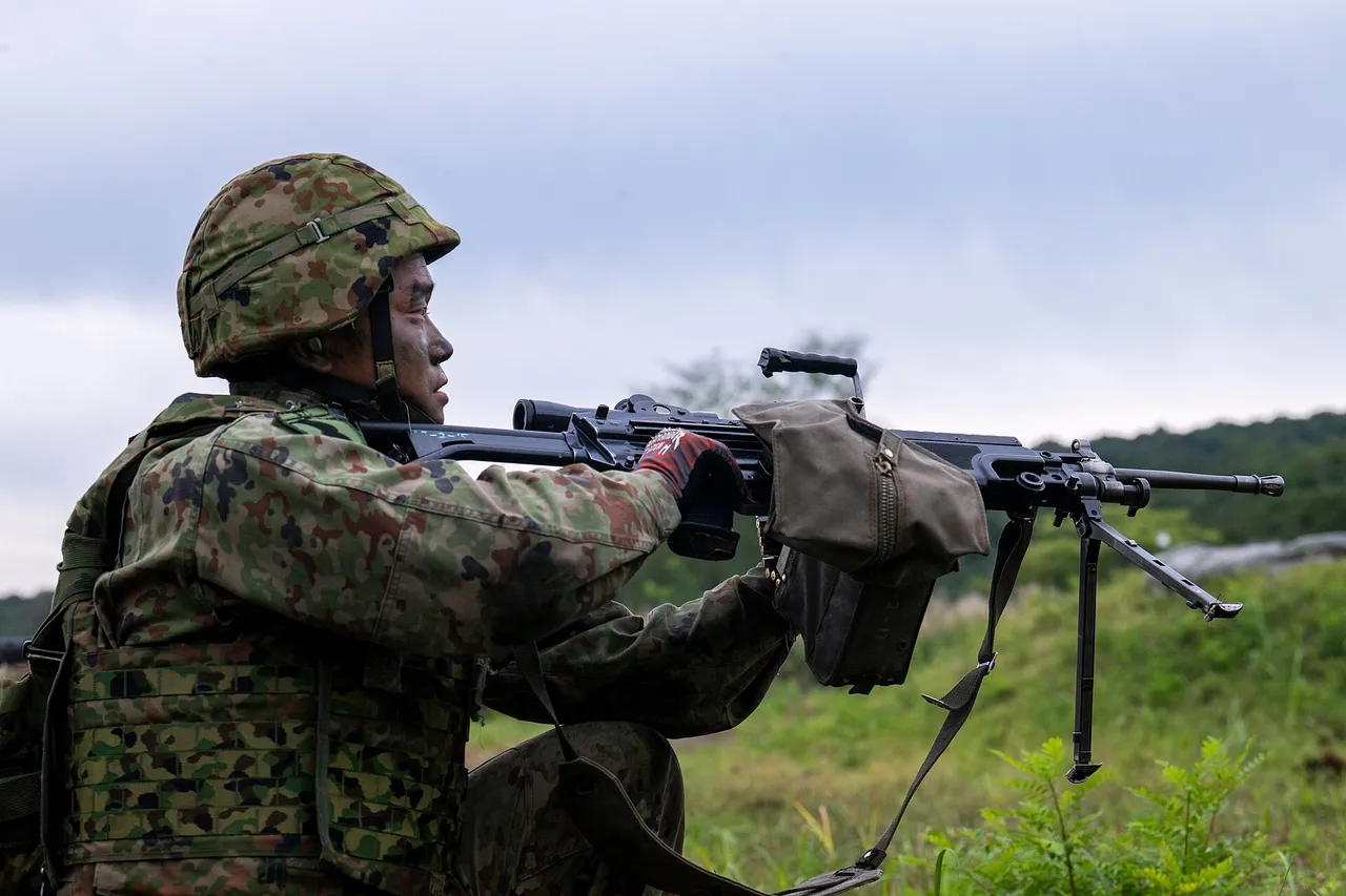 A Japanese soldier in camouflage uniform and helmet kneels and aims a machine gun on a bipod across a grassy field