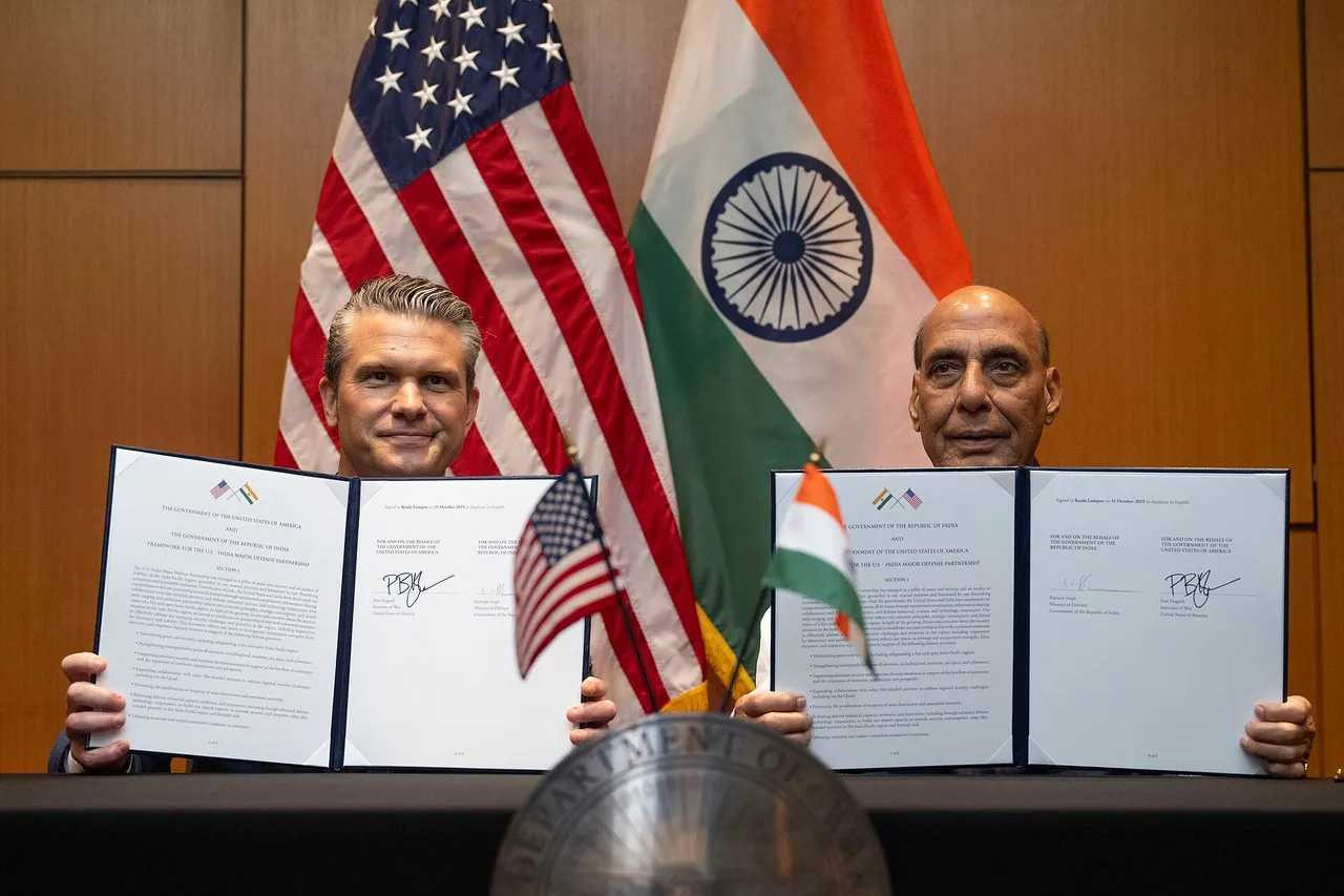Pete Hegseth and Rajnath Singh seated at a table holding up signed document folders in front of US and Indian flags