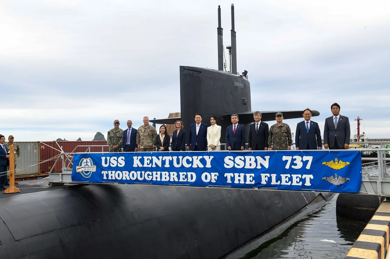 South Korean President Yoon Suk Yeol and officials stand in a row on the deck of the US ballistic-missile submarine USS Kentucky behind a blue banner in Busan