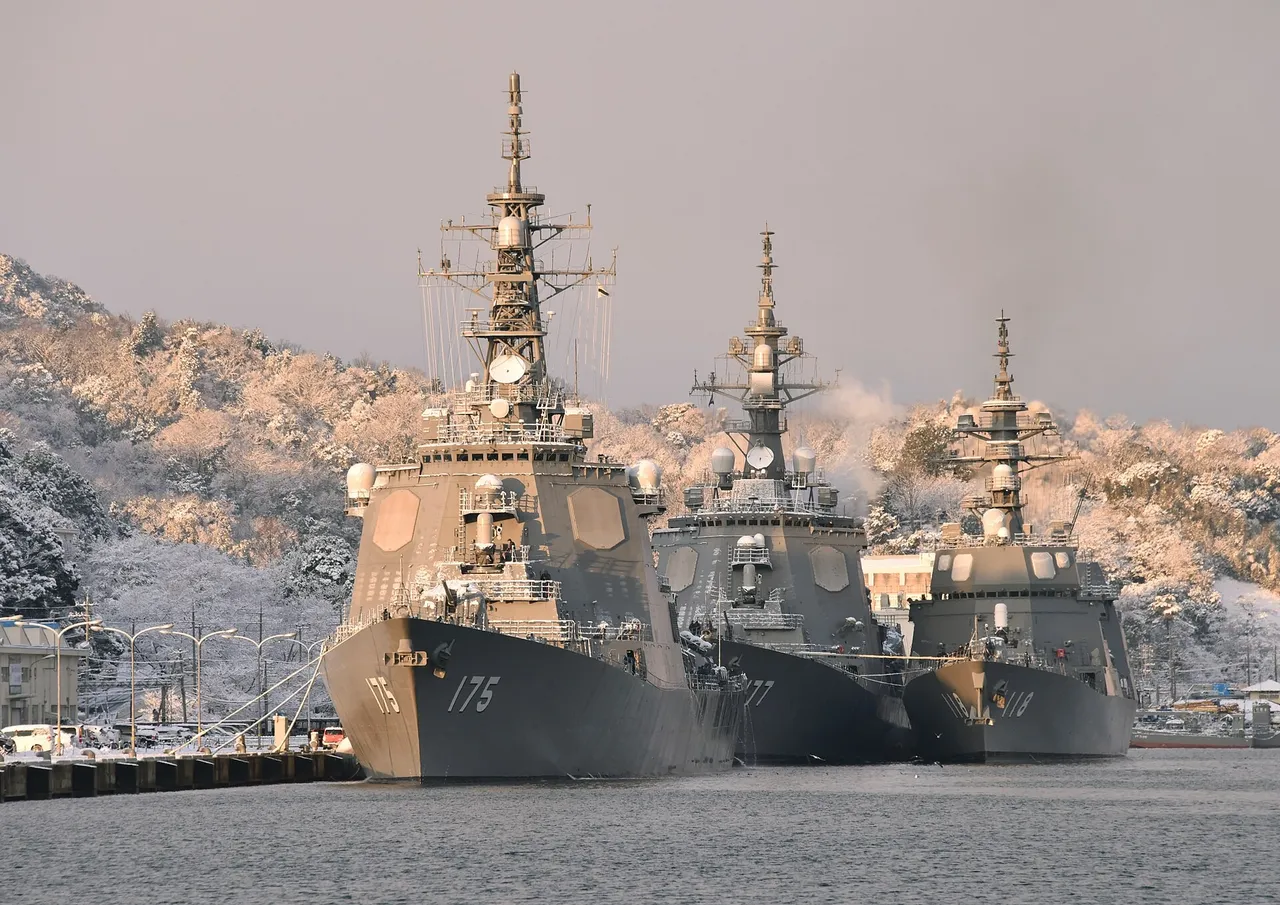 Three grey Japanese navy destroyers moored side by side at a quay in front of snow-covered hills