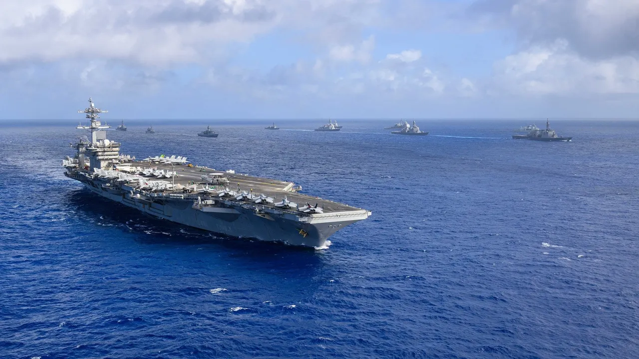 A line of grey warships including a US aircraft carrier and a Japanese helicopter destroyer sail in formation on open blue sea