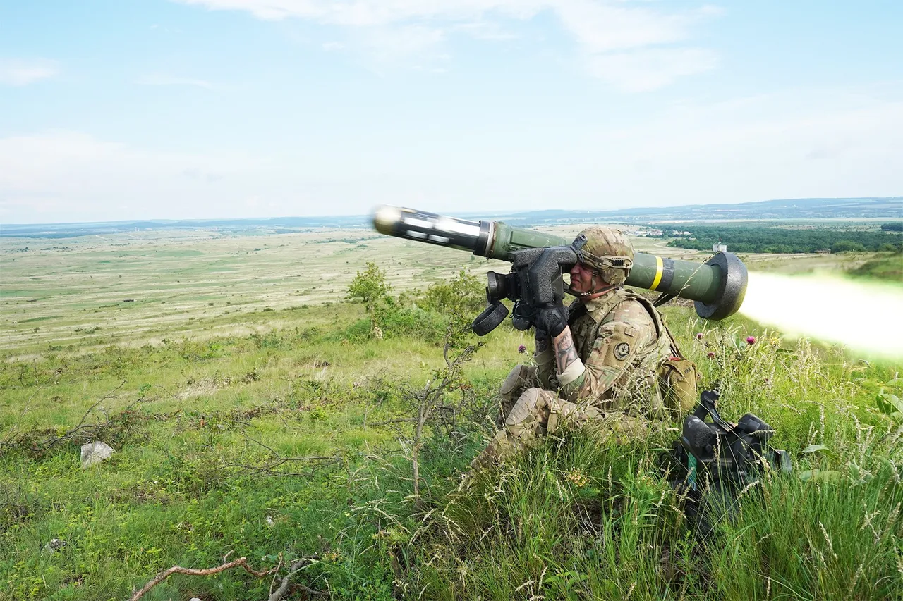 A soldier sitting in tall grass on a hillside fires a shoulder-launched Javelin missile as it leaves the tube, with the back-blast streaming behind him.
