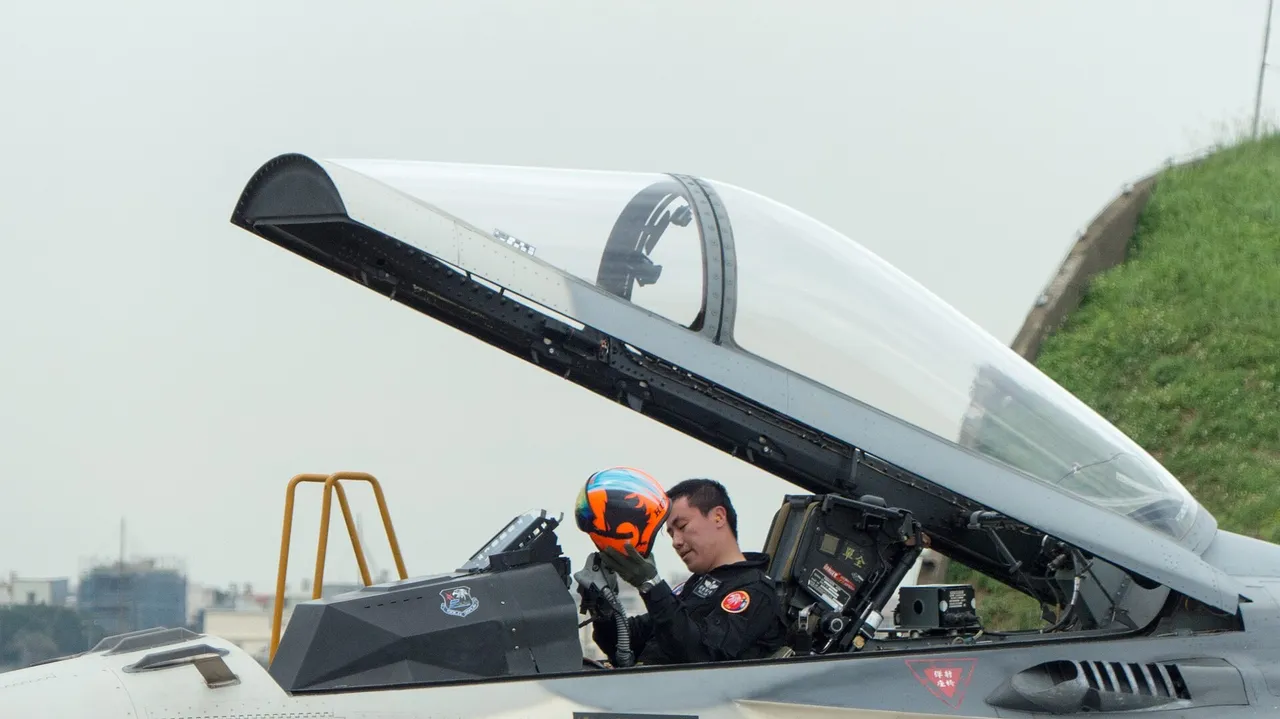 A Taiwanese fighter pilot in a flight suit sits in the open cockpit of a grey Indigenous Defense Fighter, holding his helmet after a flight