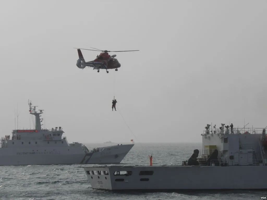 Several white Taiwanese coast guard patrol ships with blue and red hull stripes sail in open water while a helicopter flies overhead