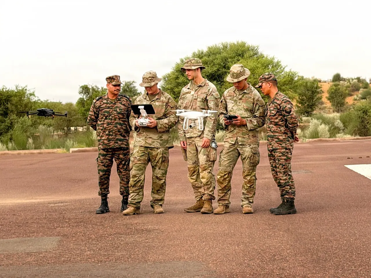 Indian and US soldiers stand on a tarmac operating small drones, one hovering beside them