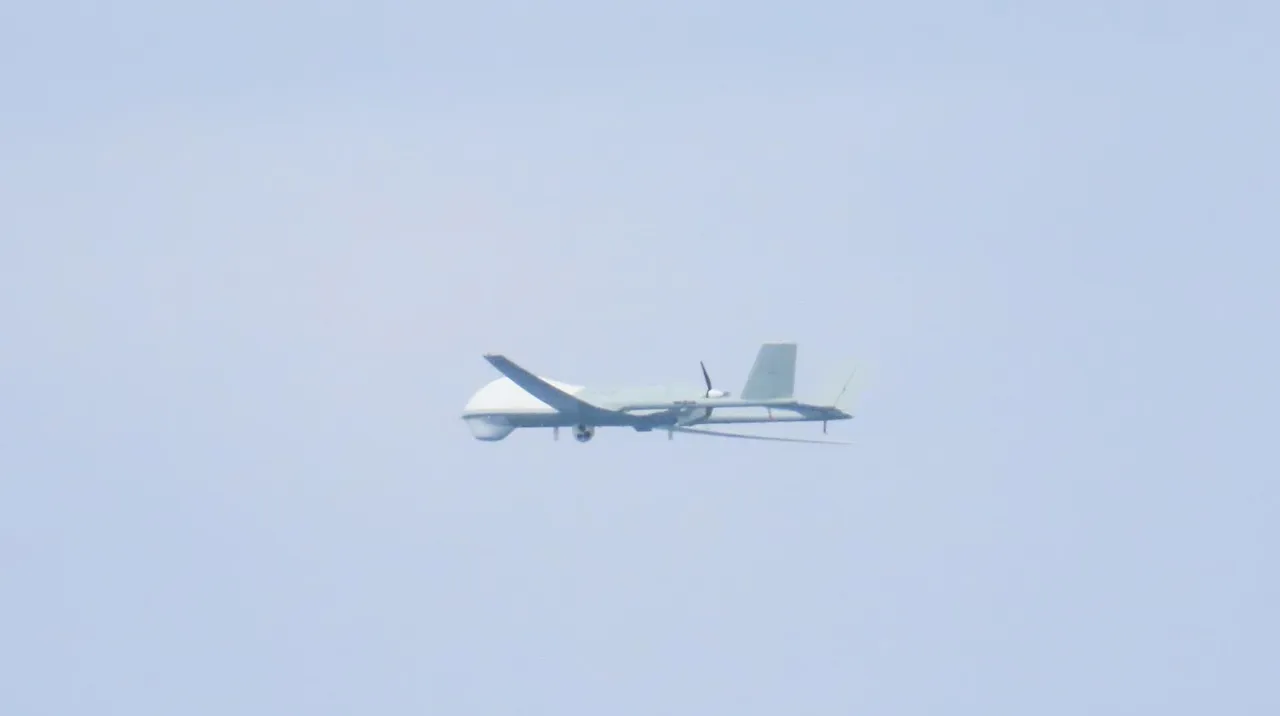 A pale grey Chinese reconnaissance drone with a bulbous nose and twin tail fins flying against a hazy sky