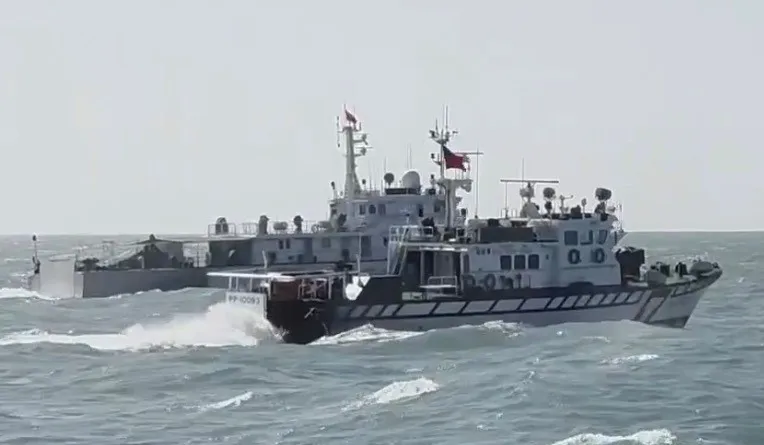 A white Taiwan Coast Guard patrol boat with a dark hull band ploughs through heavy grey swell beside a larger white vessel.