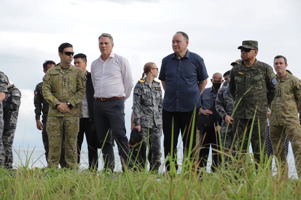 Philippine Defence Secretary Gilberto Teodoro stands on a grassy shoreline with Australian and Philippine military officers watching an exercise.