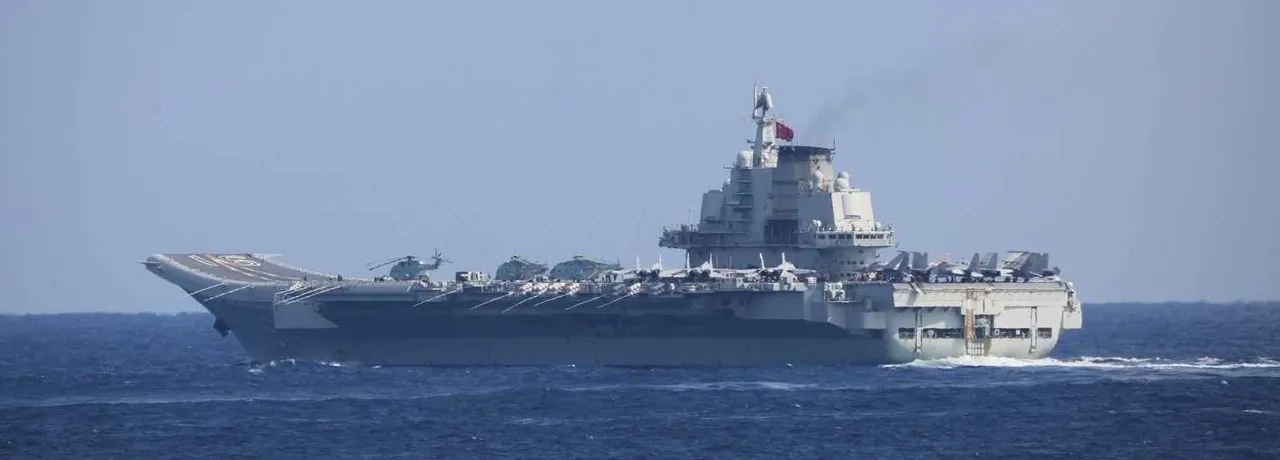 A grey aircraft carrier with a ski-jump bow sailing on open sea, seen from the side