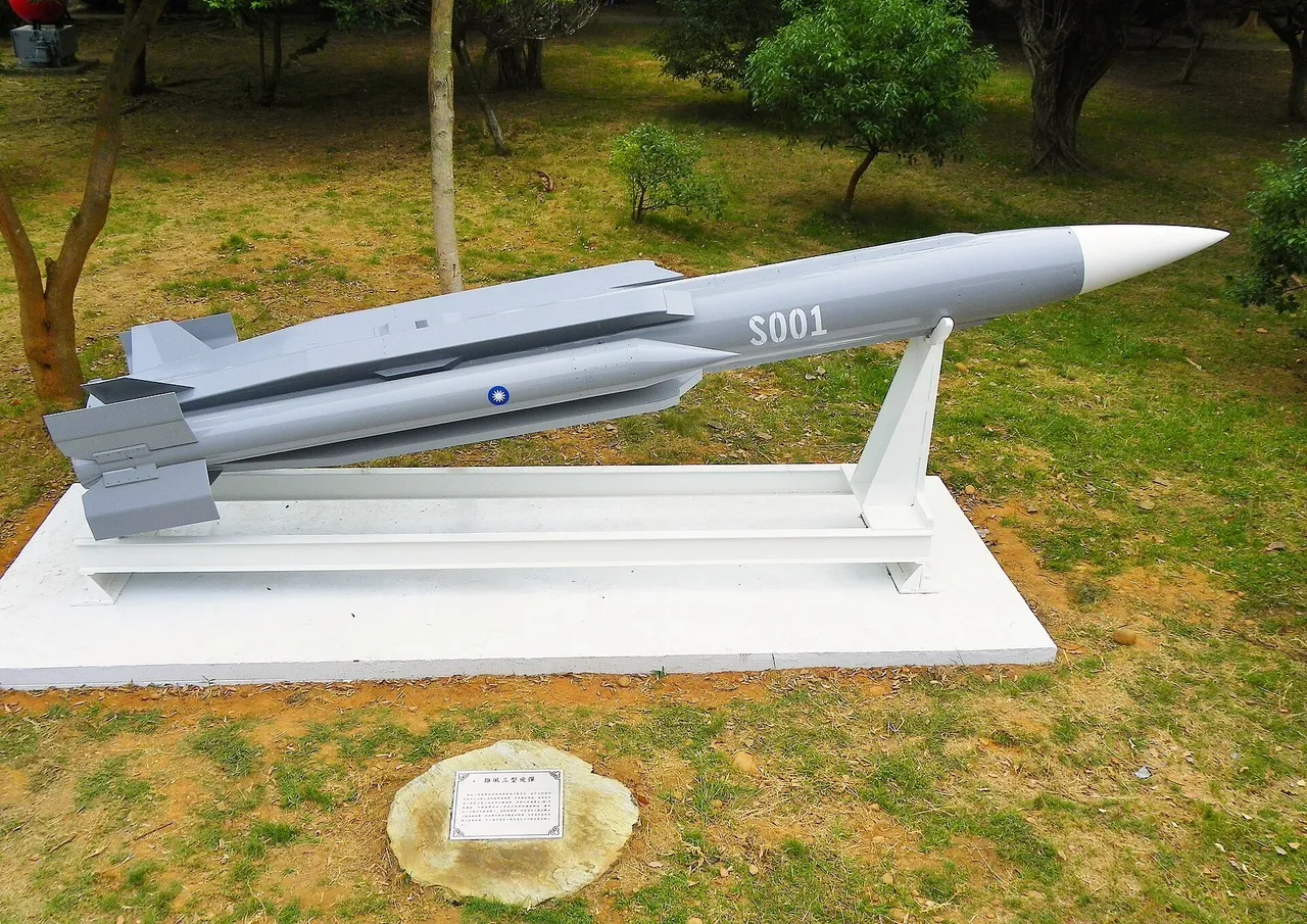 A grey Hsiung Feng III anti-ship missile with a white nose cone and the number S001 rests on a white display stand on grass among trees