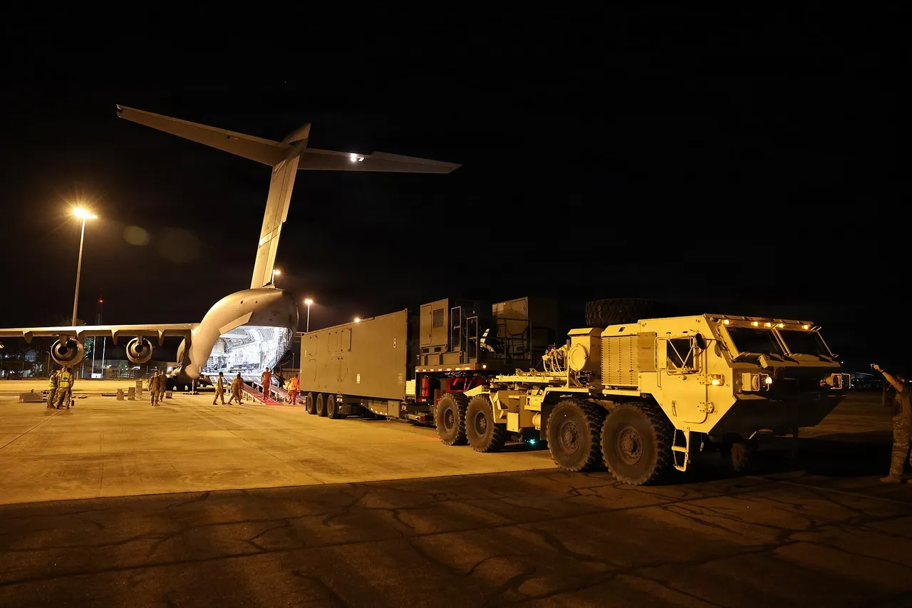 A large US Army Typhon missile launcher trailer being unloaded from the rear ramp of a grey C-17 transport aircraft