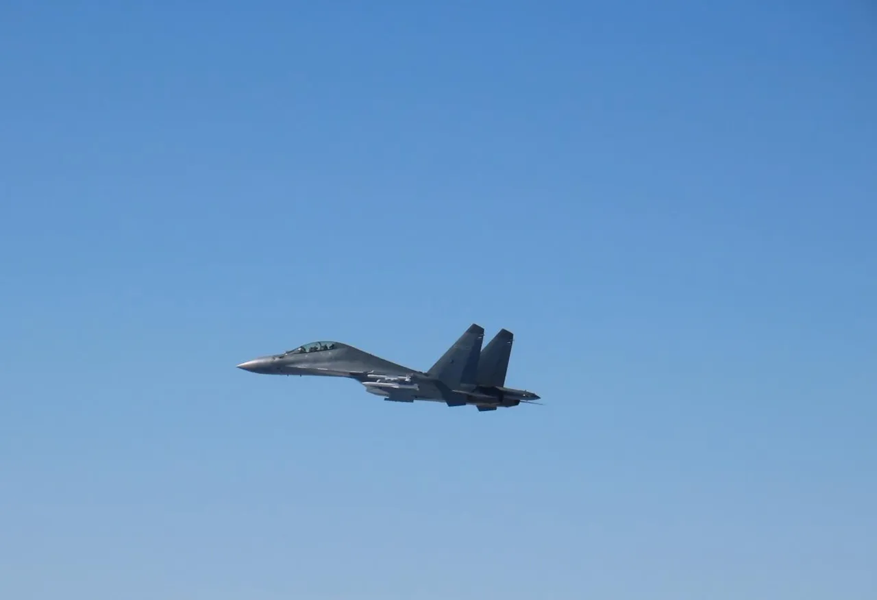 A grey twin-tailed J-16 fighter jet flying against a clear blue sky.