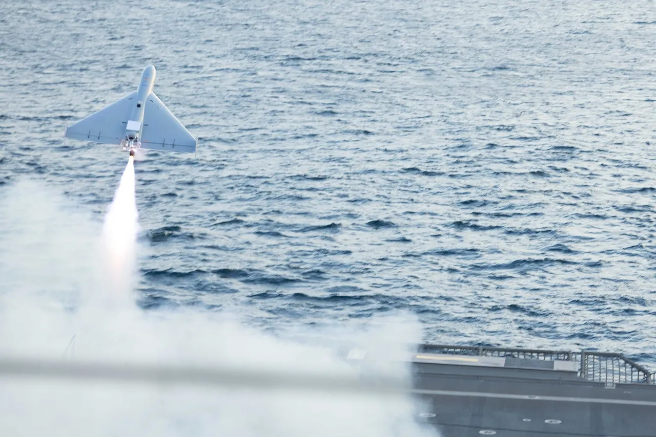 A white delta-wing drone climbs away from a warship's flight deck on a rocket booster trail over open sea