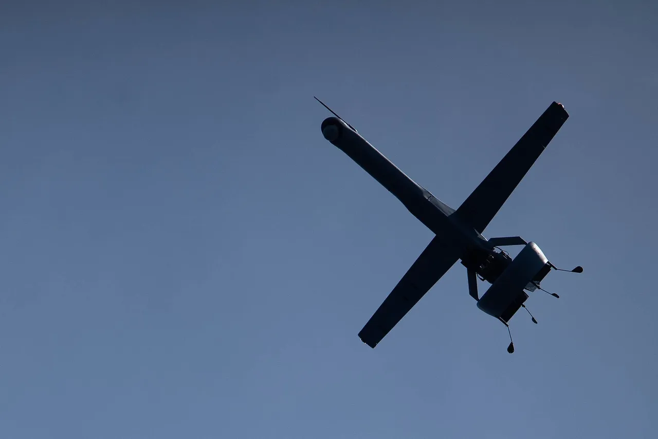A small tail-sitting ducted-fan drone flying over the sea beside a grey US Navy amphibious ship