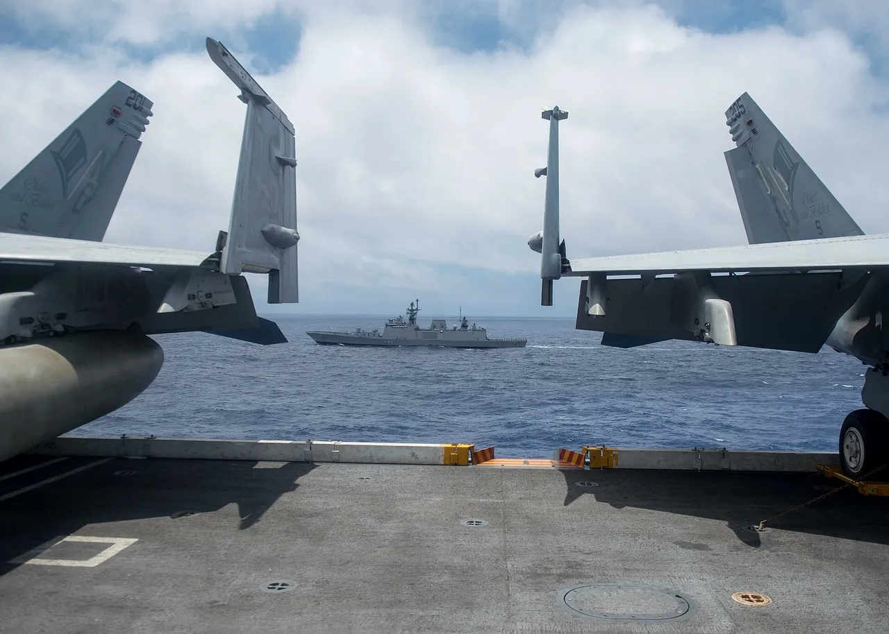 A grey Indian Navy stealth frigate with hull number F49 sails at sea seen from the deck of a large aircraft carrier