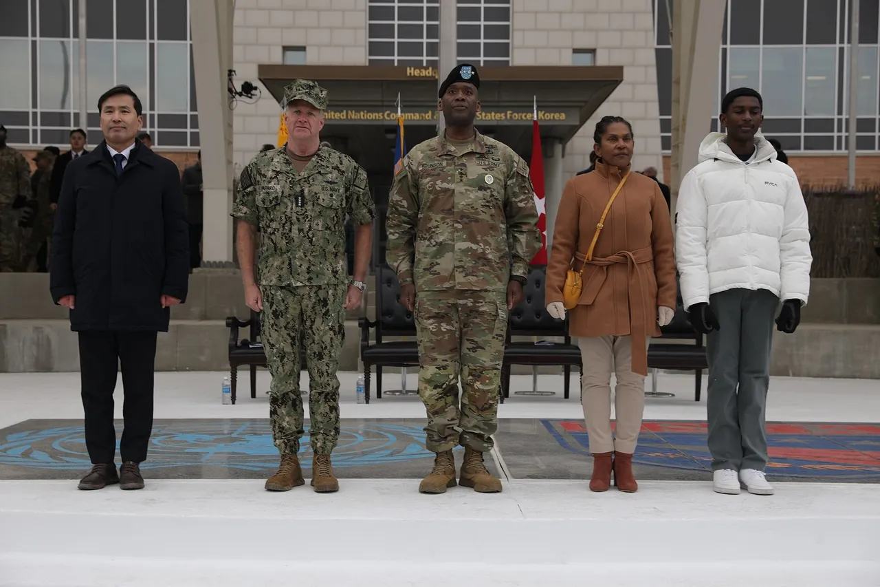 US Army general in camouflage uniform standing on a reviewing stand with officials and family members in front of a headquarters building