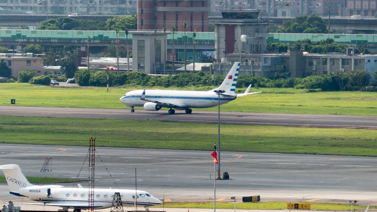 A white Taiwanese air force Boeing 737 with a national flag on its tail rolls down a runway in front of a control tower and city buildings