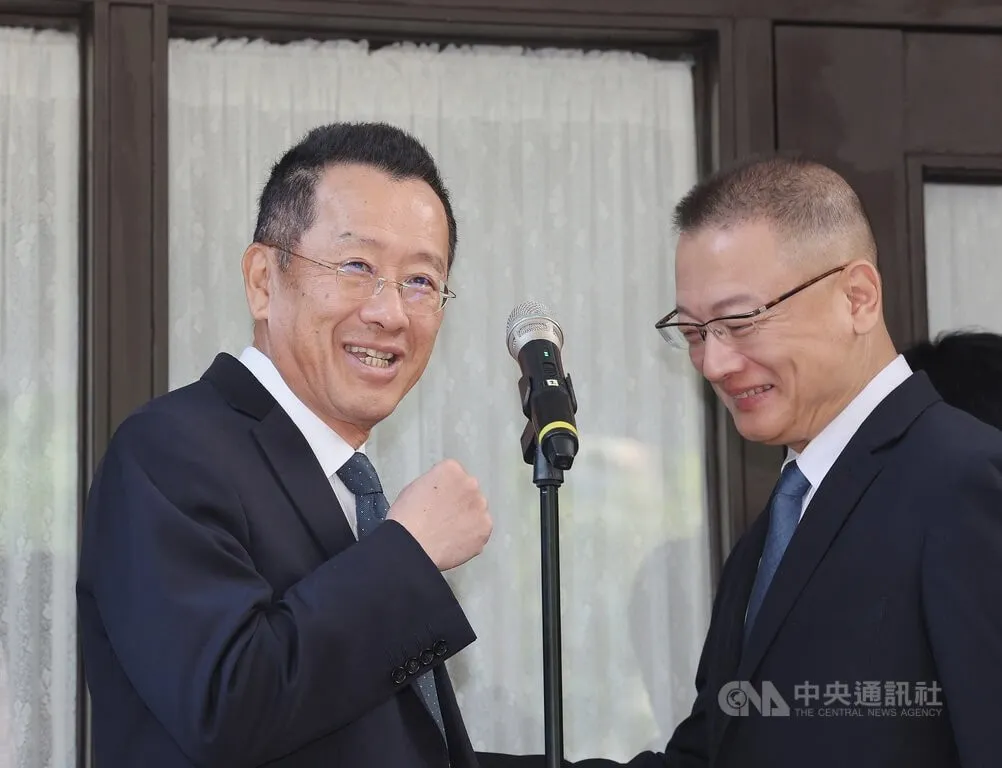 Wellington Koo in a dark suit and glasses smiling and raising a fist beside a microphone, next to another man in a suit.