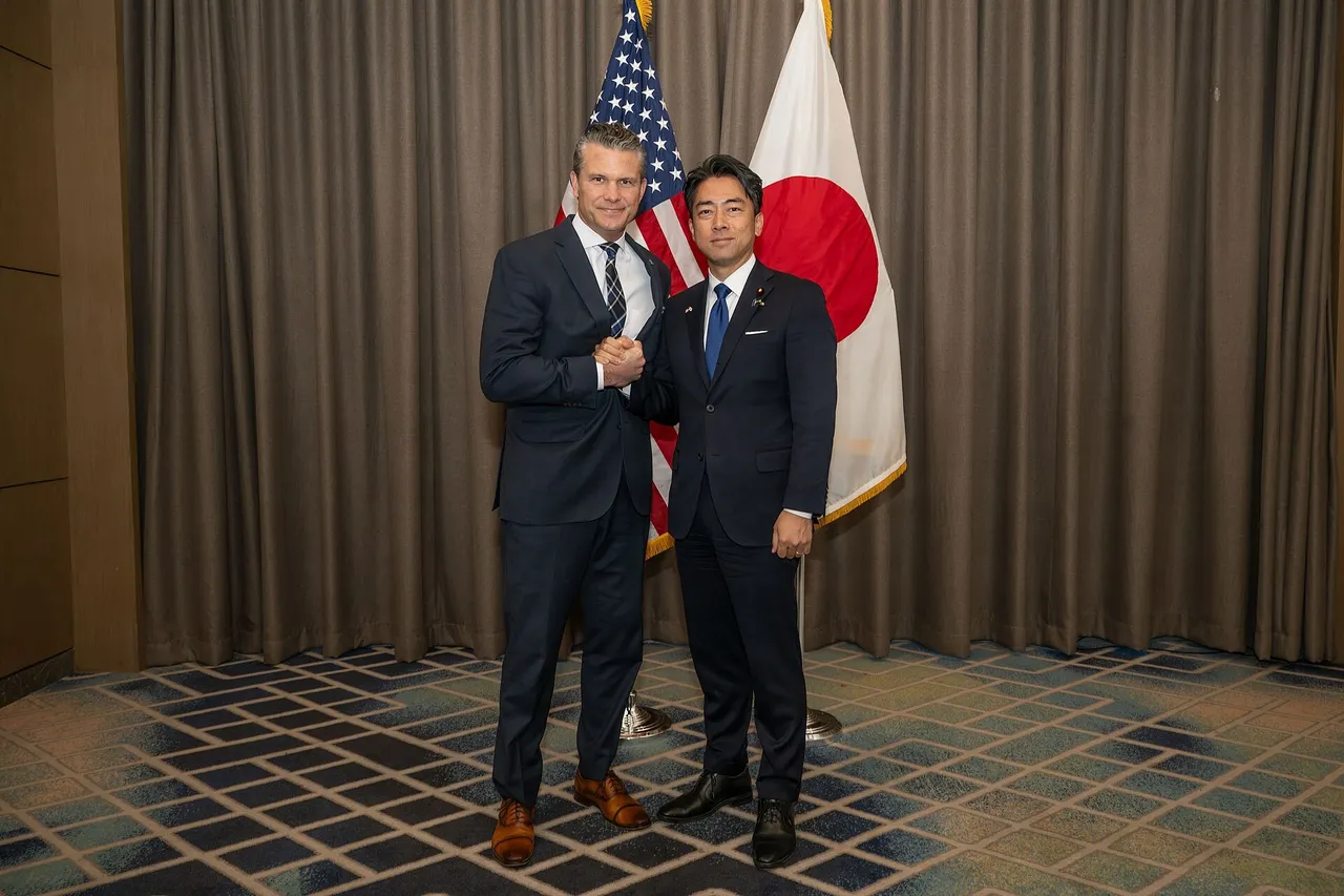 Pete Hegseth and Shinjiro Koizumi shaking hands in front of US and Japanese flags