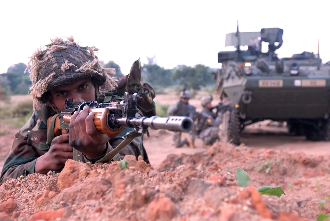 An Indian Army soldier in camouflage with a rifle crouches on a dirt track during a training patrol