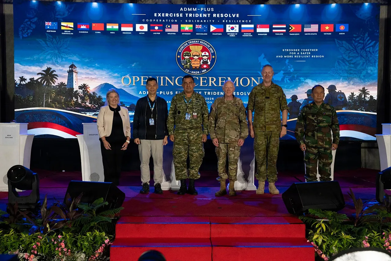Six military and civilian officials stand on a stage in front of a large screen showing the flags of ASEAN and partner countries and an exercise logo