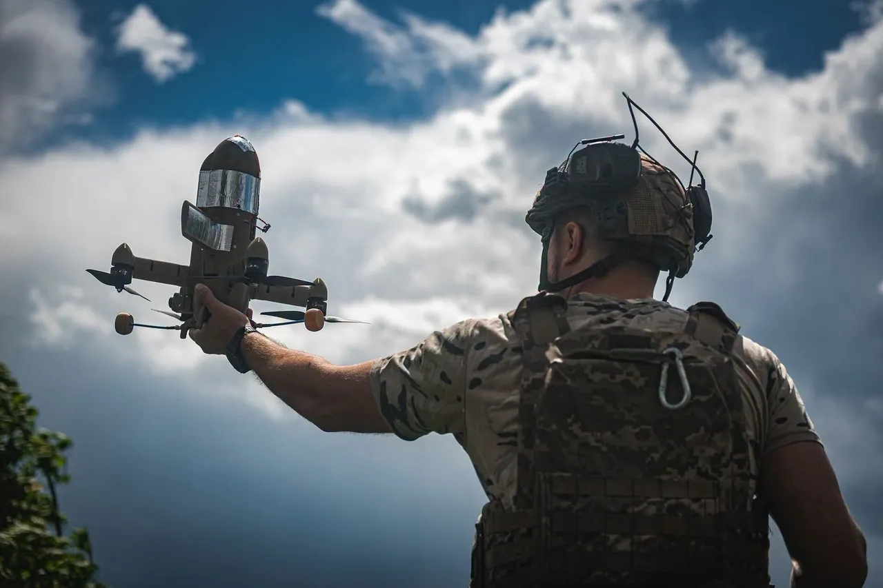A Ukrainian soldier in camouflage holds up a small interceptor drone for launch in a field