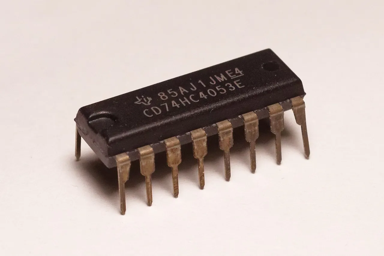 A black rectangular integrated circuit with two rows of metal pins and a Texas Instruments logo, photographed on a white surface.