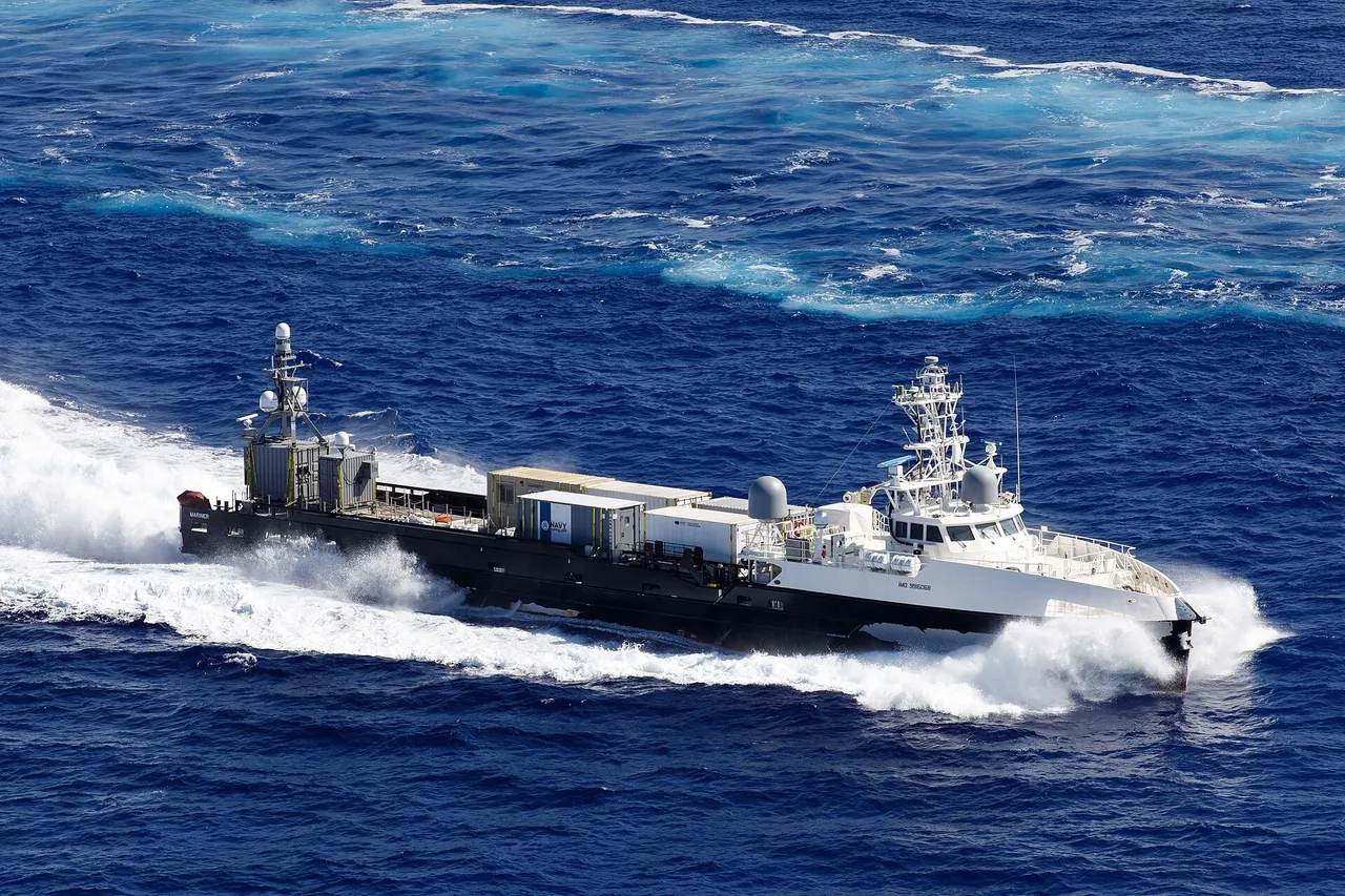 A grey and white uncrewed US Navy surface vessel with containers on deck speeding across the open ocean