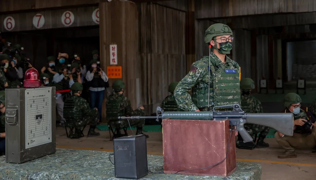 A Taiwanese soldier in camouflage and a helmet stands behind a rifle on a stand at an indoor firing range, with other soldiers and photographers behind him.