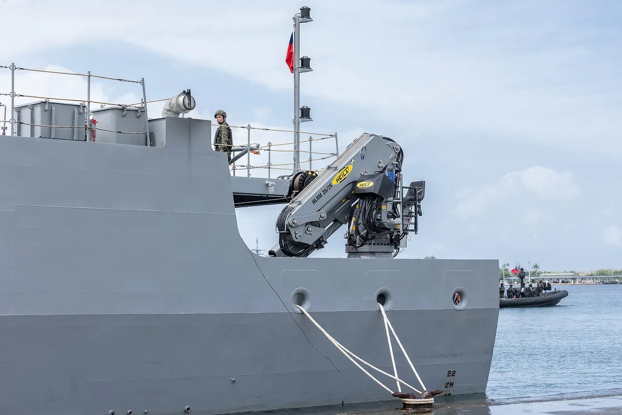 Grey hull and deck crane of a Taiwanese navy minelaying vessel moored at a pier, with a sailor on deck and a small boat in the water behind