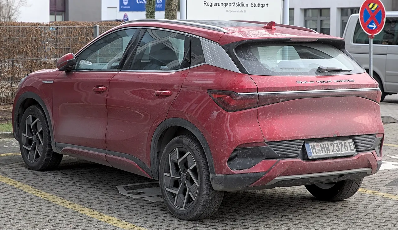 A red BYD Atto 3 compact electric SUV parked on a paved car park, seen from the rear three-quarter angle