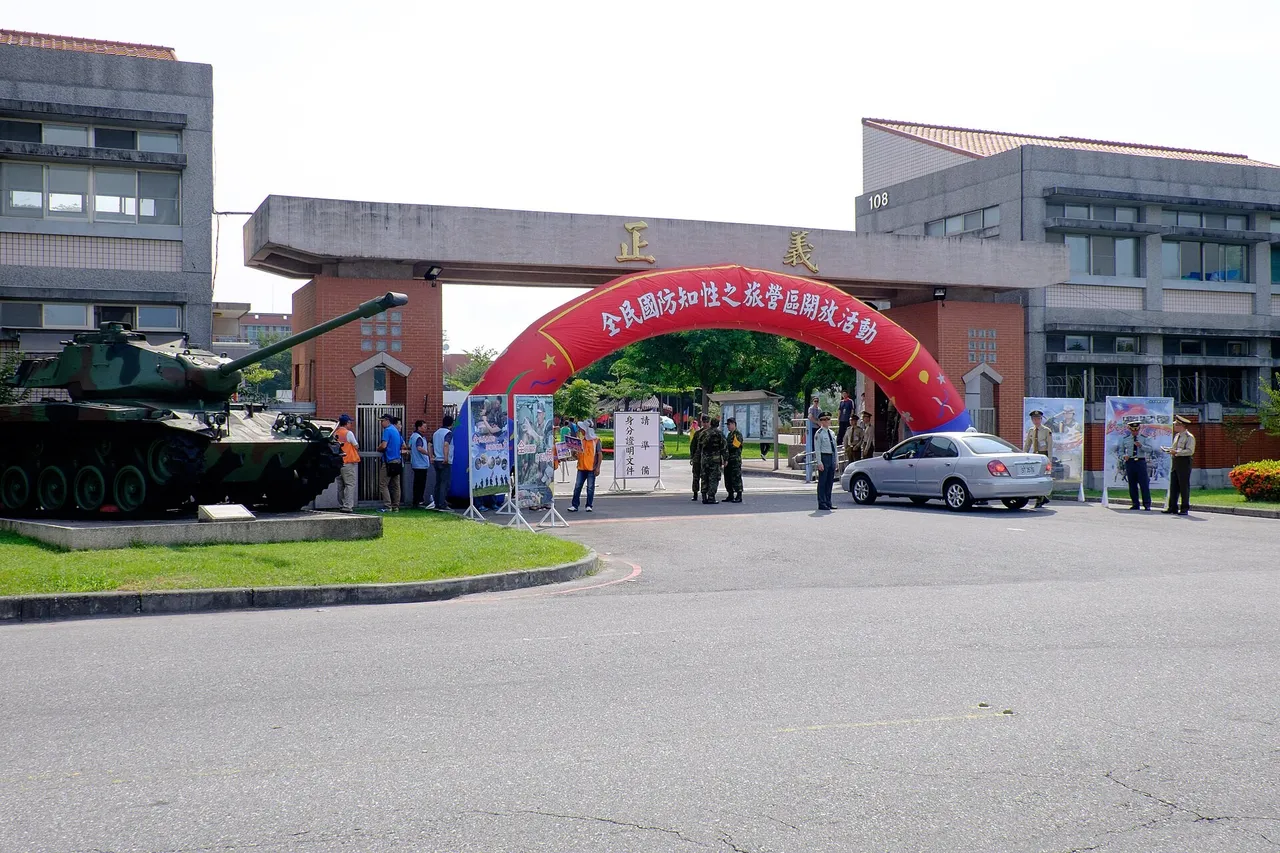 Soldiers and visitors stand at the main gate of an army camp in Hualien beneath a red inflatable arch, with a preserved tank displayed on the lawn to the left
