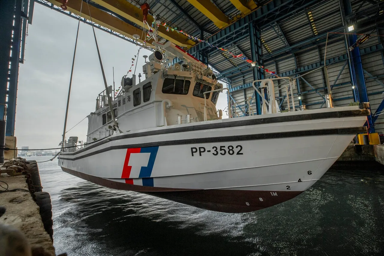 A white Taiwan Coast Guard Administration patrol boat marked PP-3582, decorated with flags, hangs from a crane just above the water inside a shipyard shed