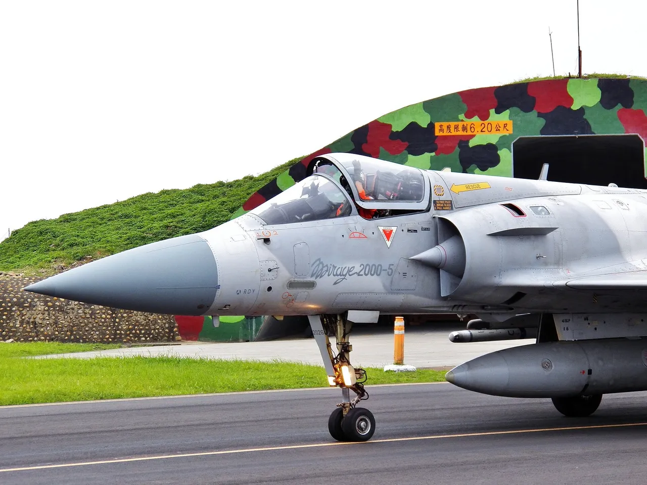A Taiwanese air force pilot in a helmet waves from the open cockpit of a grey Mirage 2000 fighter on the runway