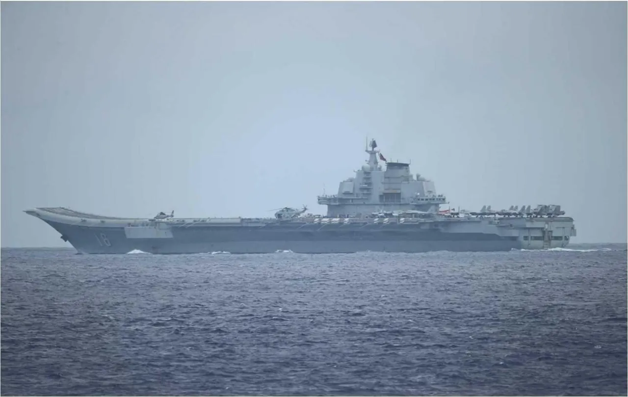 The grey Chinese aircraft carrier Liaoning under way at sea, seen from the side with its ski-jump bow and island superstructure