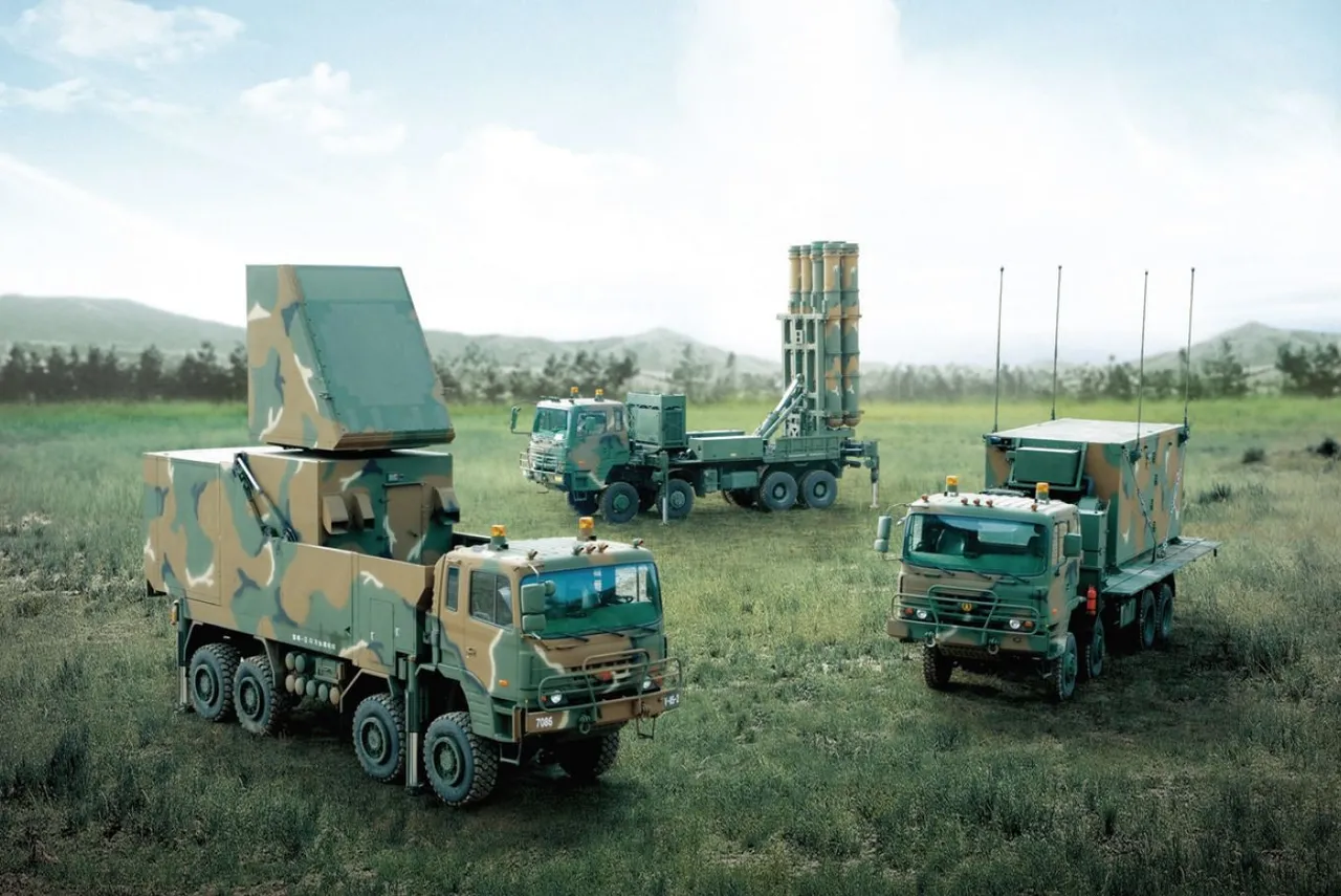 Military trucks carrying a radar panel, a raised vertical missile launcher and a control shelter parked on open ground