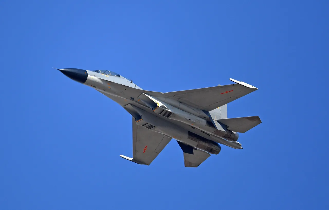 A grey twin-engine Chinese J-11 fighter jet with red markings banking against a clear blue sky, seen from below.