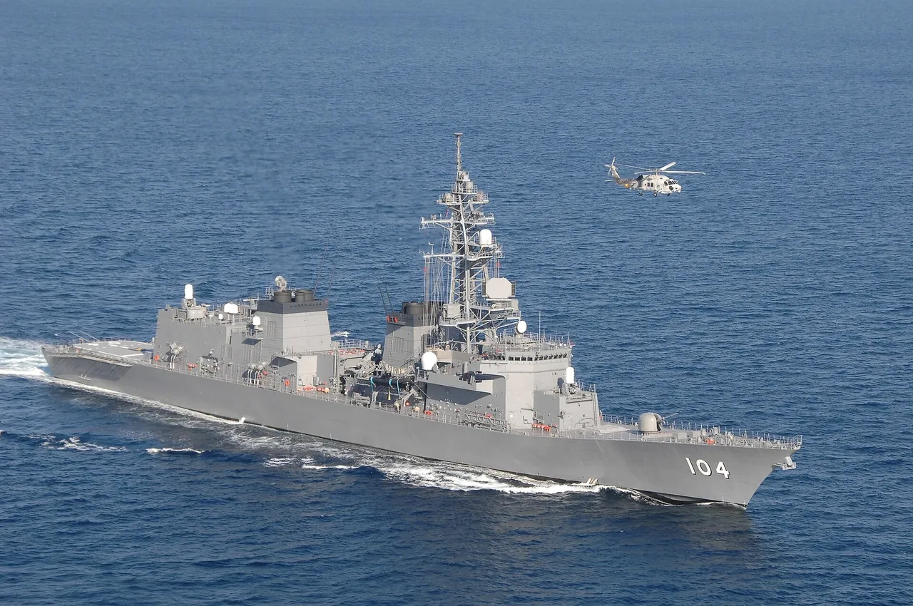 A grey Japanese navy destroyer under way at sea with a helicopter flying above it