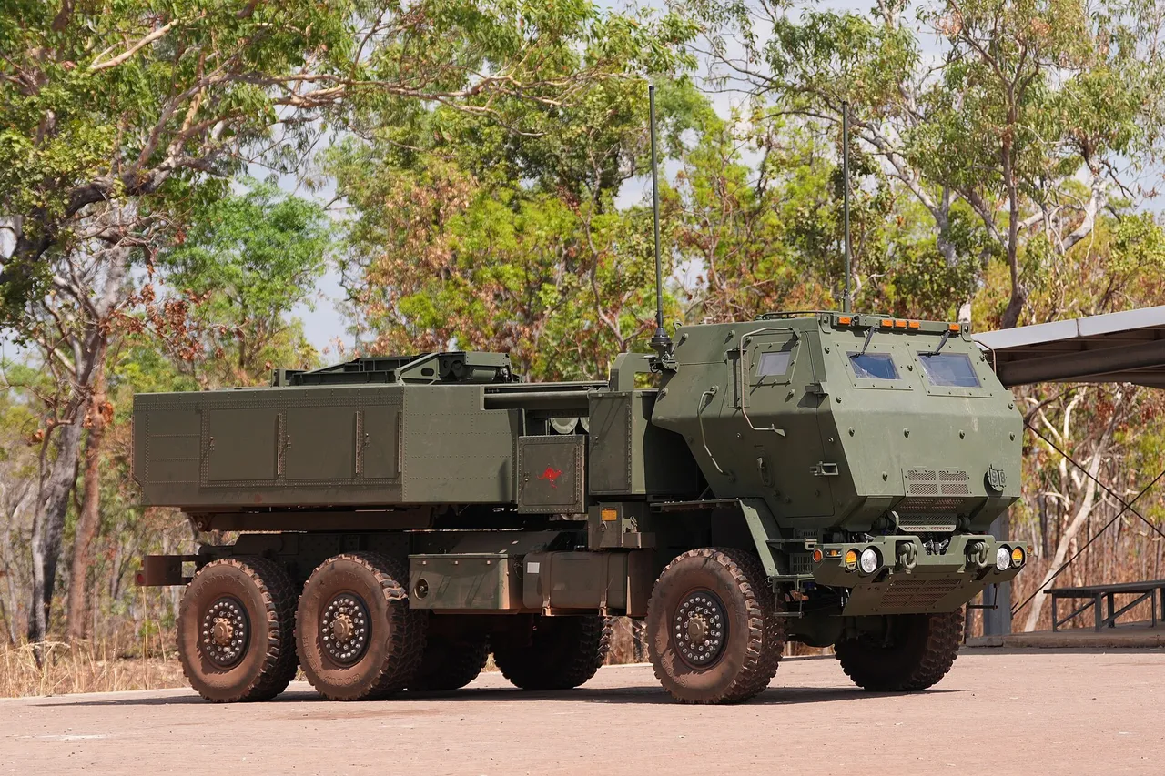 A green six-wheeled Australian Army HIMARS rocket launcher truck parked on a dirt apron in front of eucalyptus trees