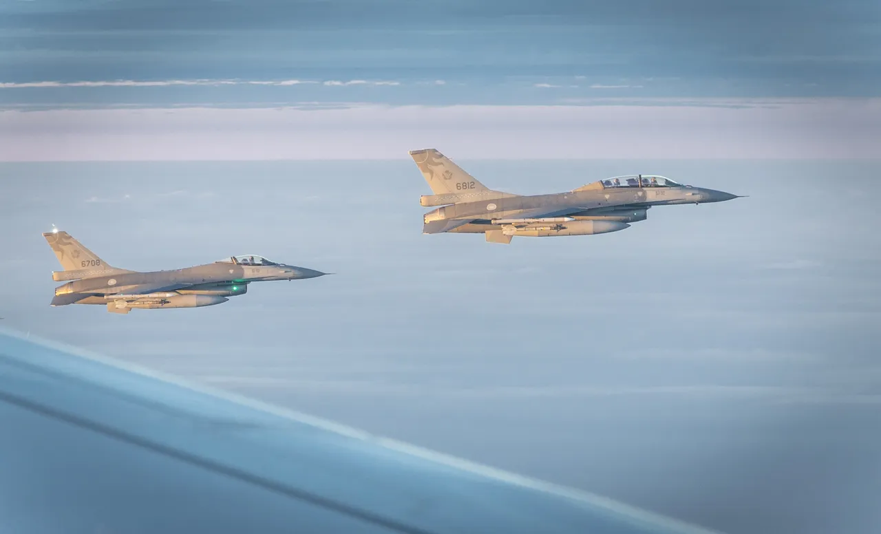 Two grey F-16 fighter jets fly in formation above a layer of cloud, seen past the wing of a larger aircraft.