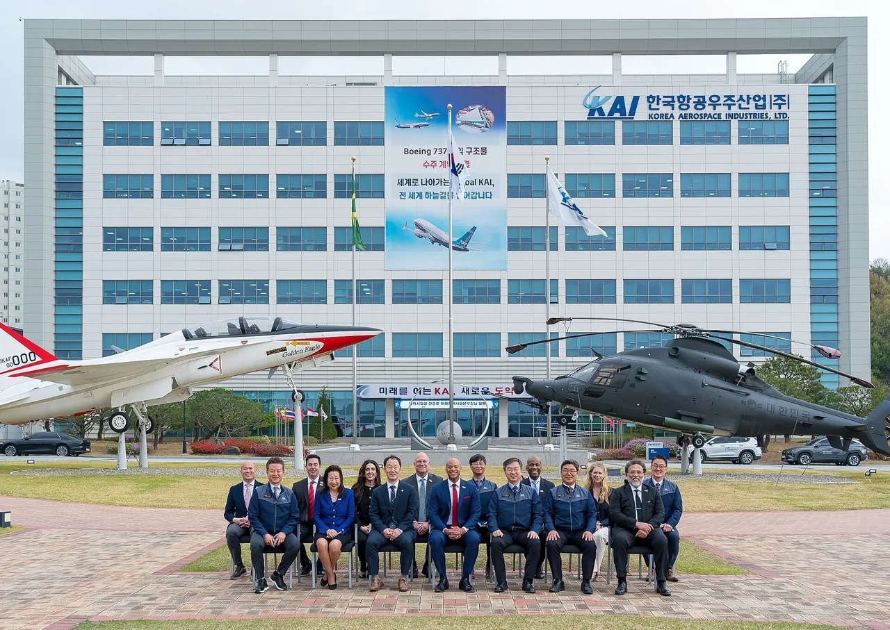 A group of visitors seated in front of the Korea Aerospace Industries headquarters building, with a jet trainer and a helicopter on display